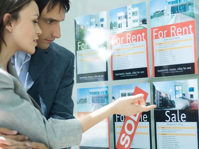 Two people looking at For Rent and For Sale property signs in a window