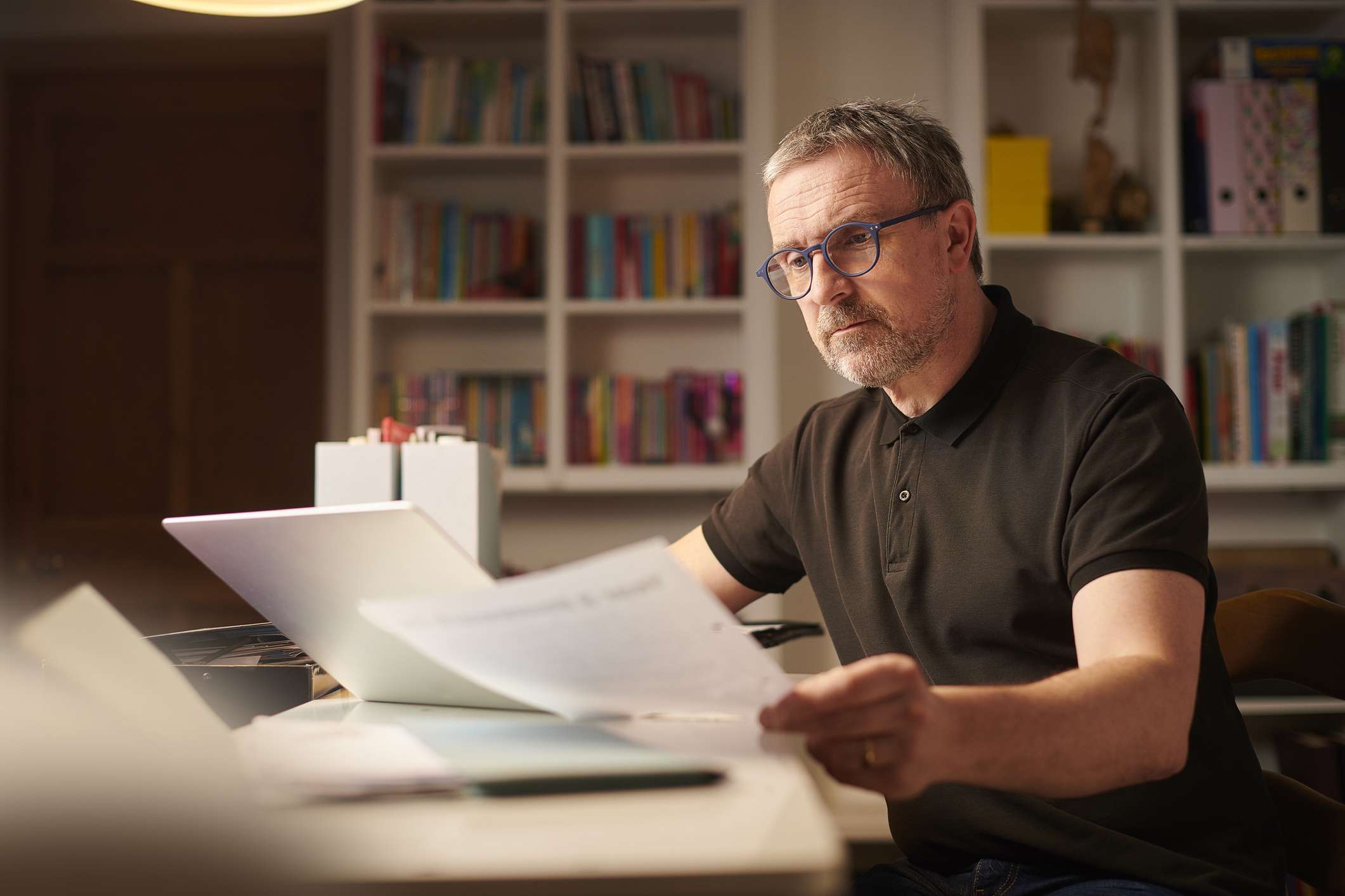 A man reviews paperwork in his home at night.