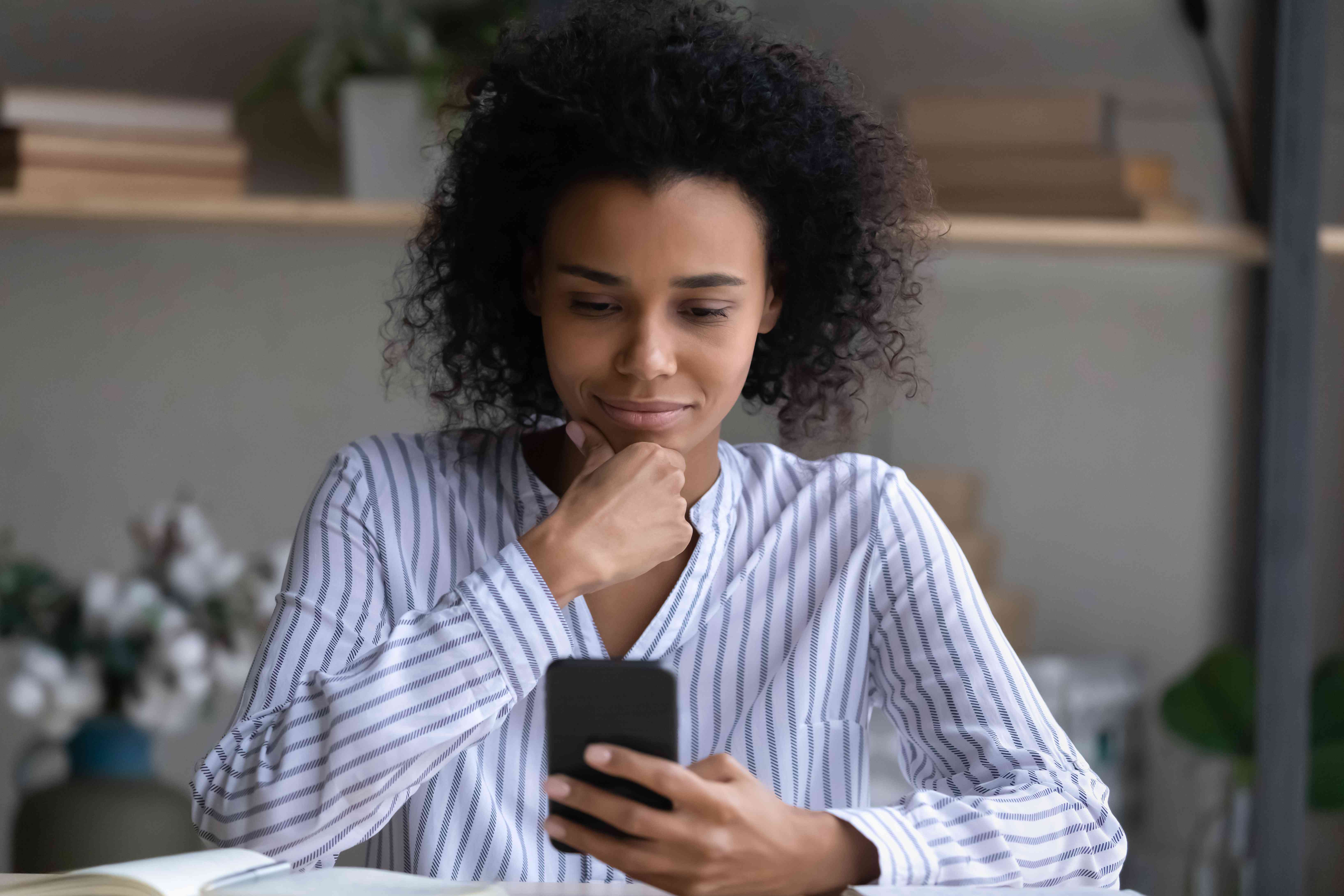 Young woman at home, pondering something on her smartphone with a slight smile