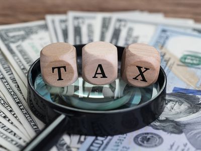 Cube wooden blocks with word TAX on a magnifying glass on US dollar banknotes on a wood table.