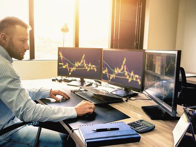 Young trader is working at stock market with three computer screen on his office desk.