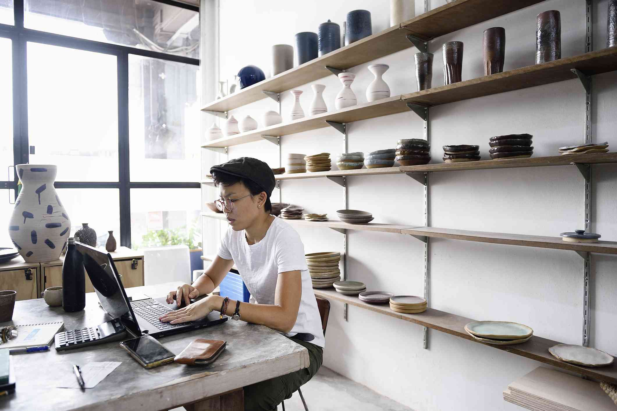 Person working on a laptop at a small pottery business