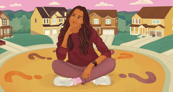 Person with long, dark hair sits cross-leg in a neighborhood thinking about their home buying dream.