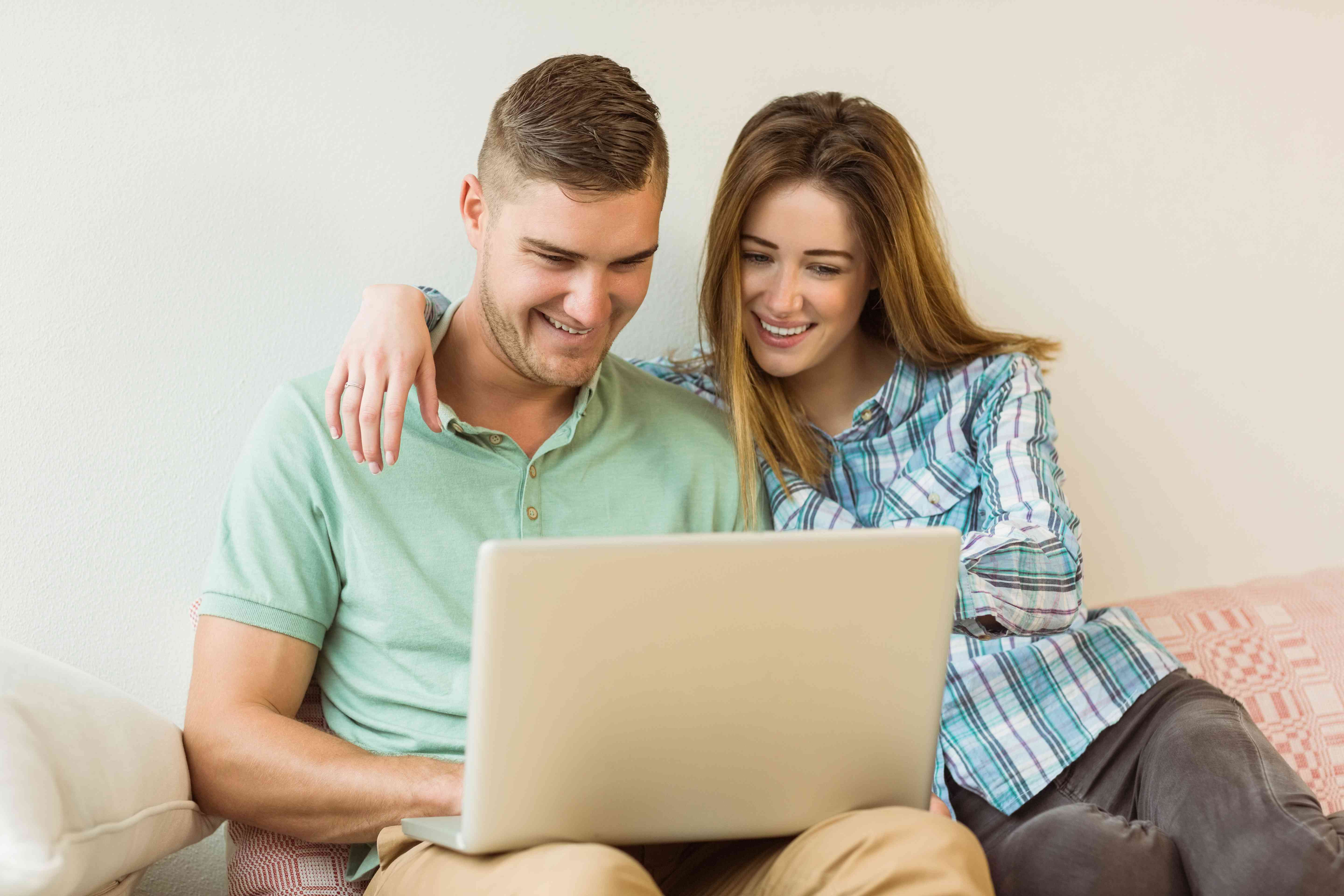 Young couple sitting together on living room couch and smiling as they look at a laptop screen