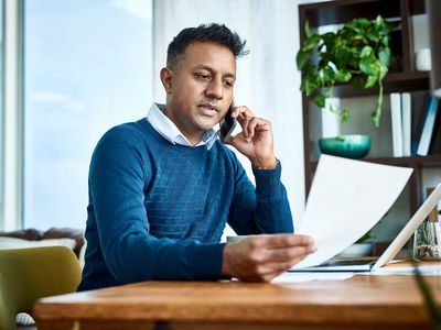 A man talks on the phone while holding documents.