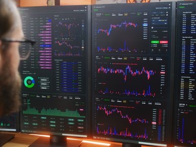 A trader sitting in front of several computer screens showing candlestick charts and other data.