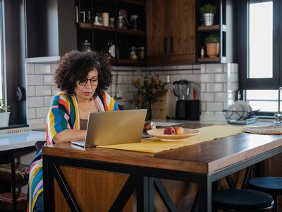 A woman in a colorful sweater sits at a kitchen island with a laptop