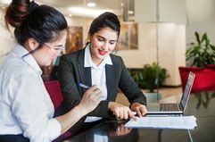 Woman in a business suit with a laptop helping a client sign papers