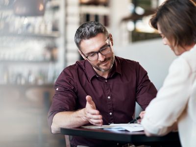 Two adults sitting at a table discuss documents.