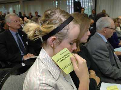 A shareholder contemplates their actions as they hold their voting card while attending an annual shareholders meeting