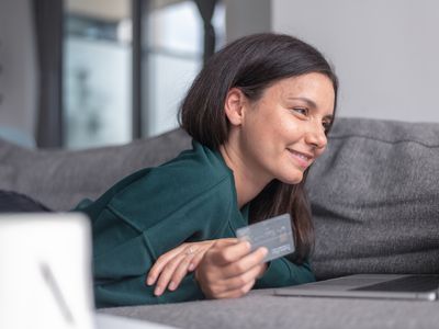 A smiling woman relaxes on the couch, holding a bank card.