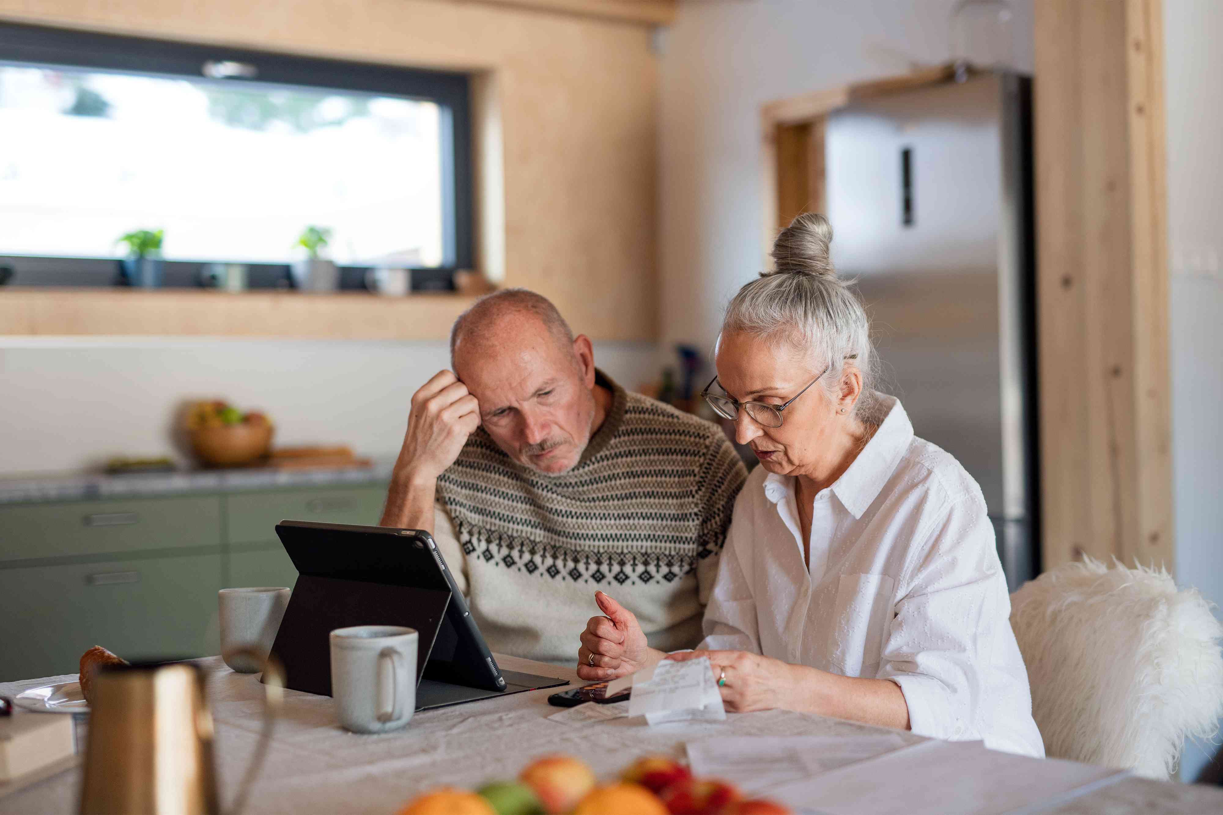 enior couple sitting at the kitchen table looking at digital tablet and recalculating their expenses because of inflation