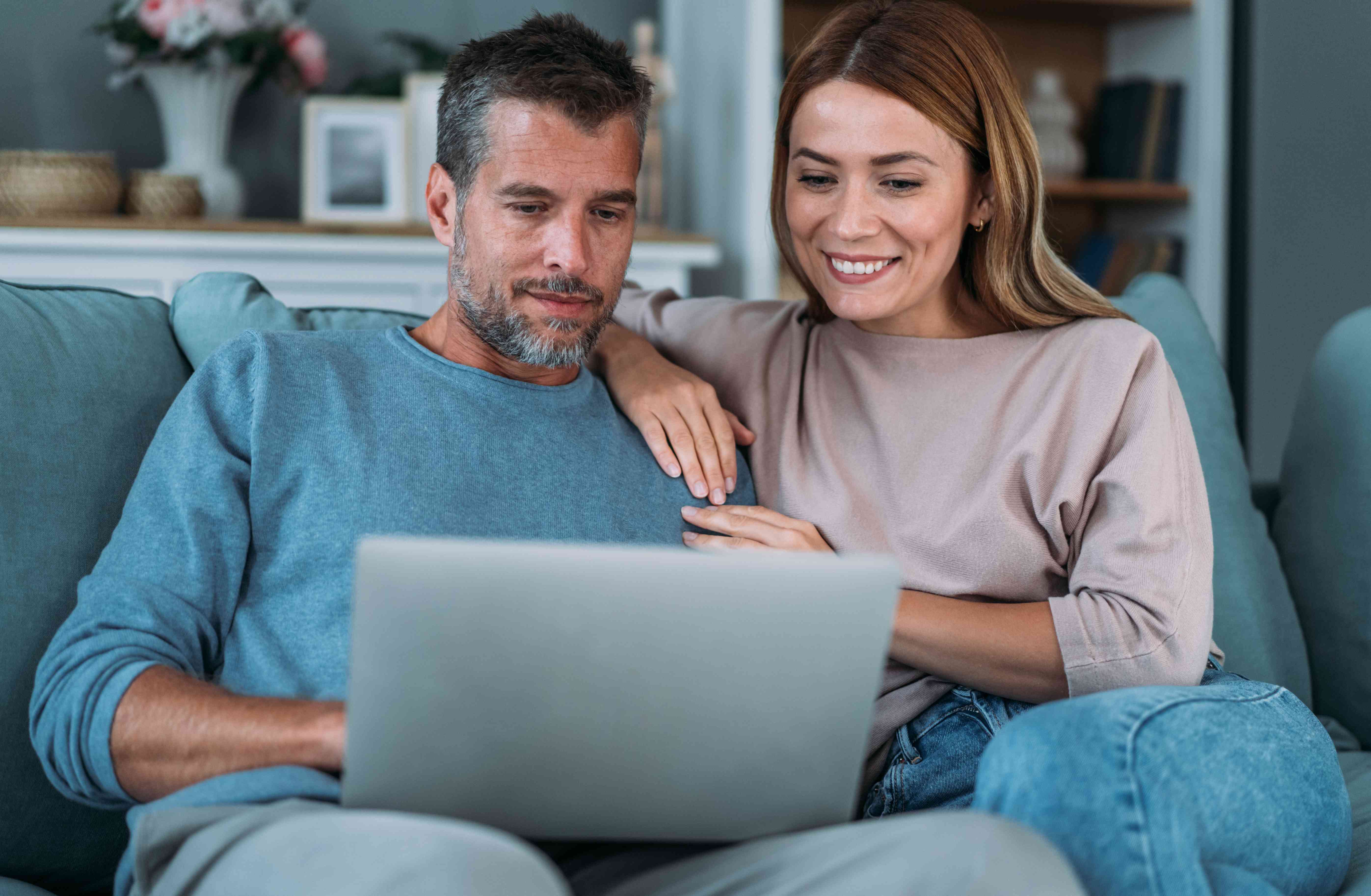 Couple in their 30s or 40s sitting on their living room couch and looking together at a laptop