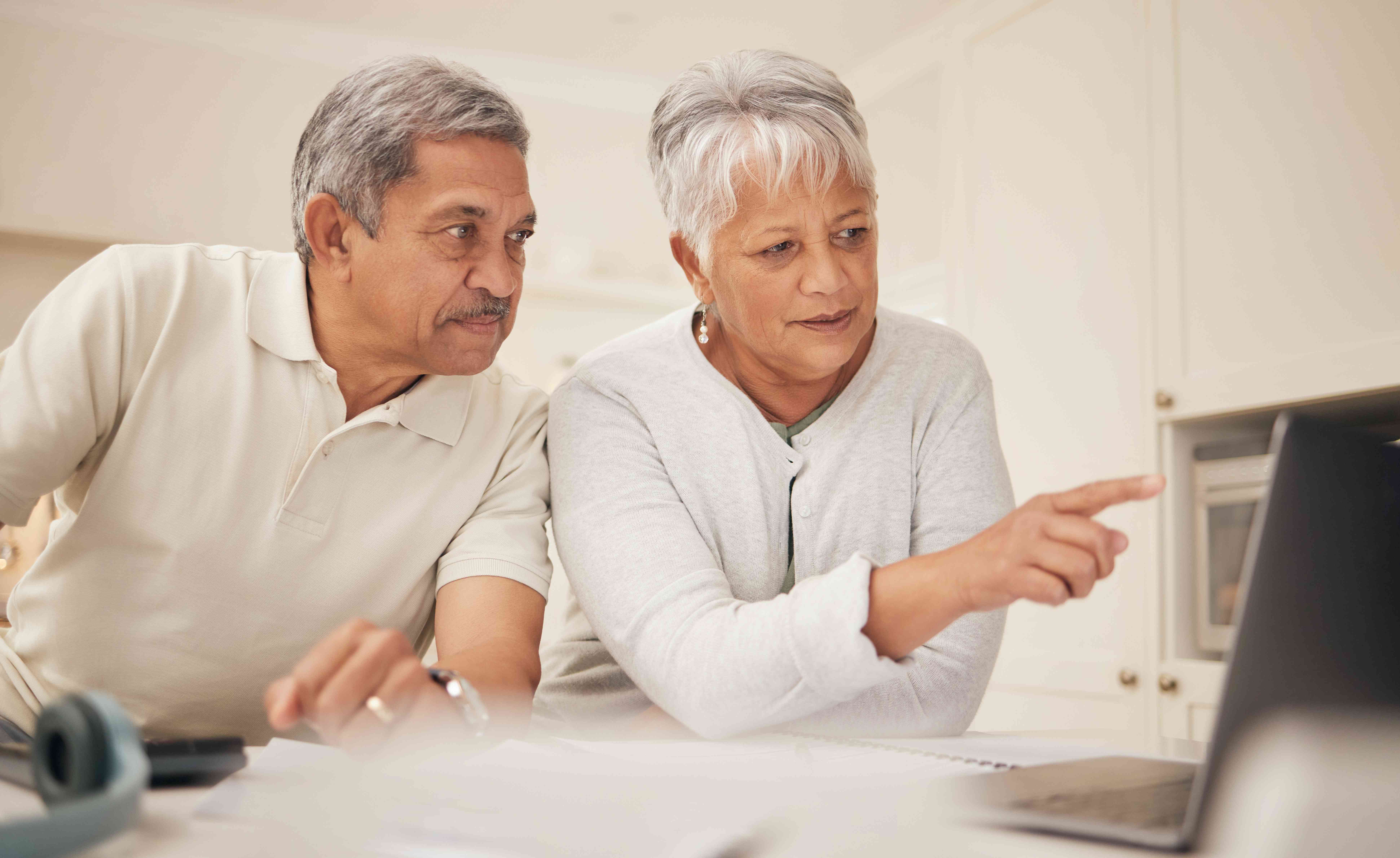 Older couple at their kitchen table, looking together at information on a laptop