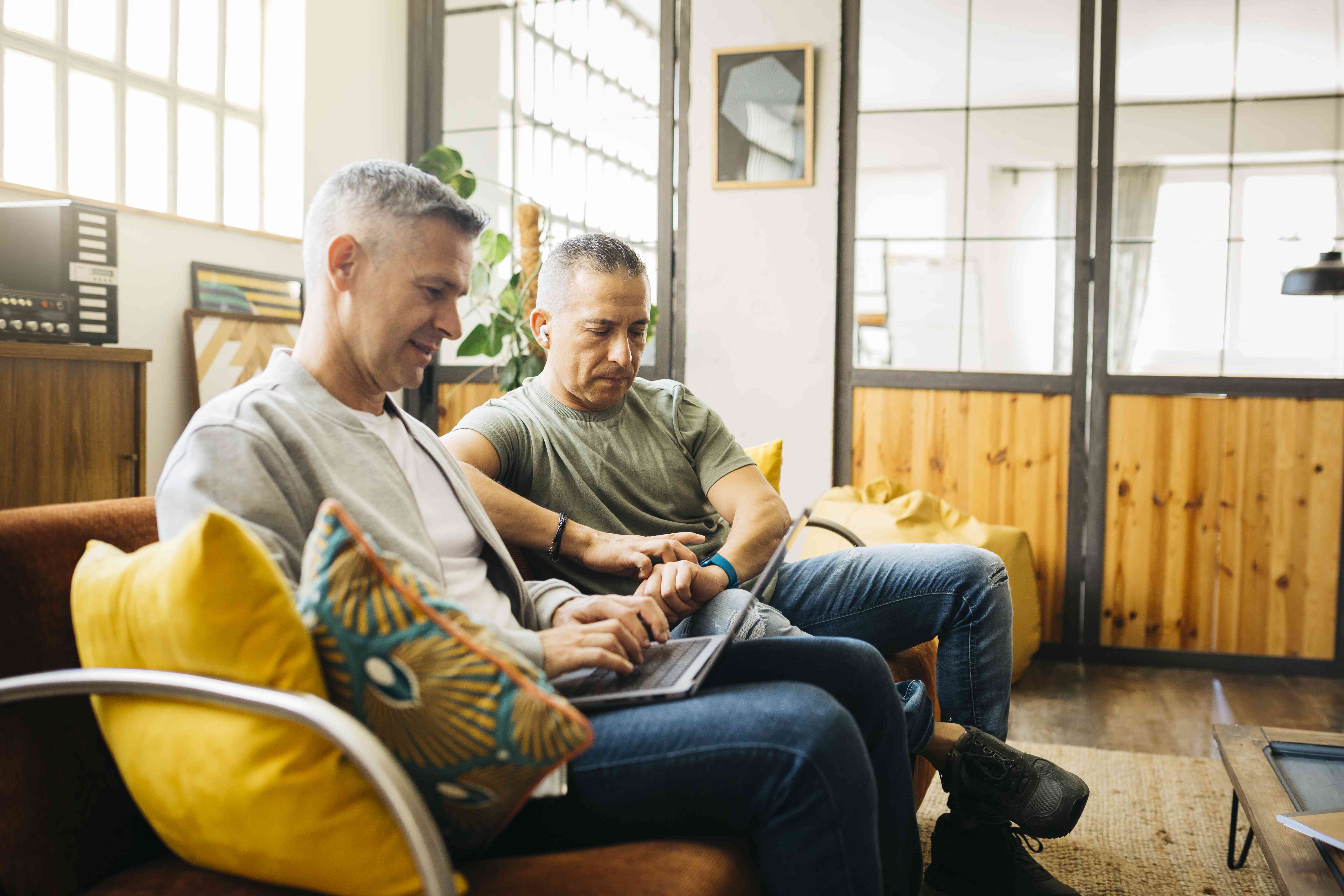 A couple sits on a couch looking at a laptop.