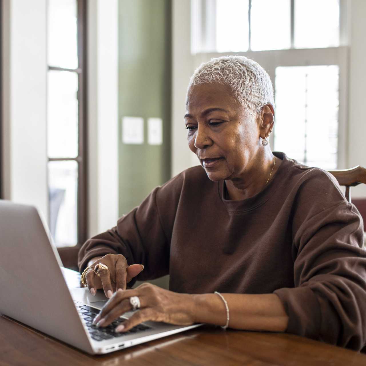 Woman in a brown sweater sitting at a wood table on a laptop