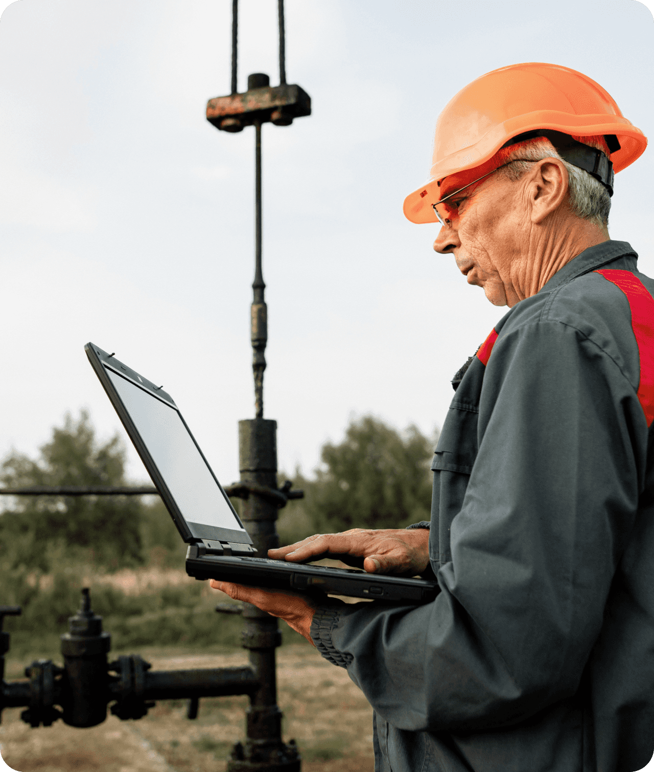 Man in outdoor construction setting wearing a hard hat and using a laptop