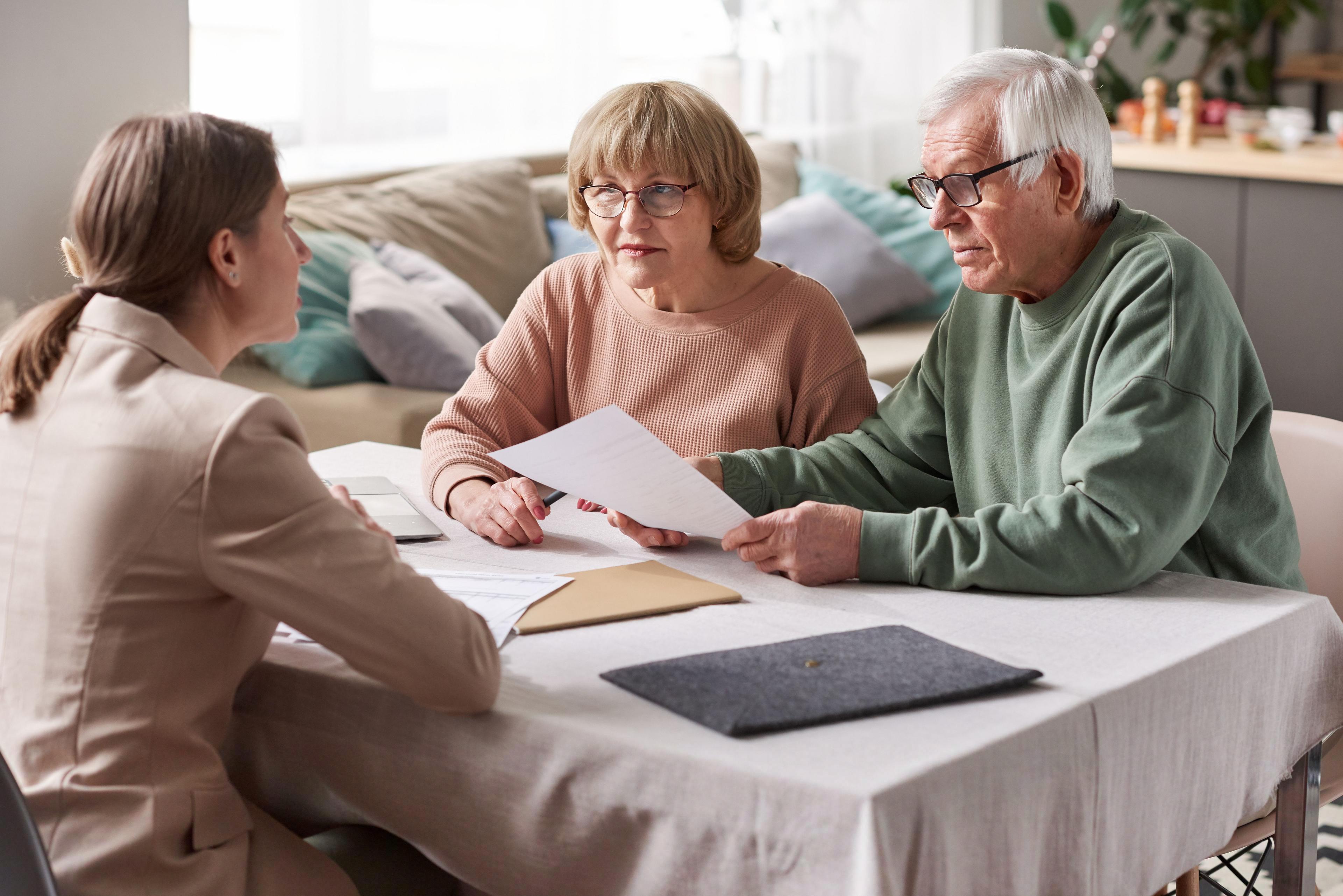 An elderly couple is having a serious discussion with a financial consultant at a table, looking at documents. This scene represents split testing for pricing strategies in financial planning or real estate transactions.