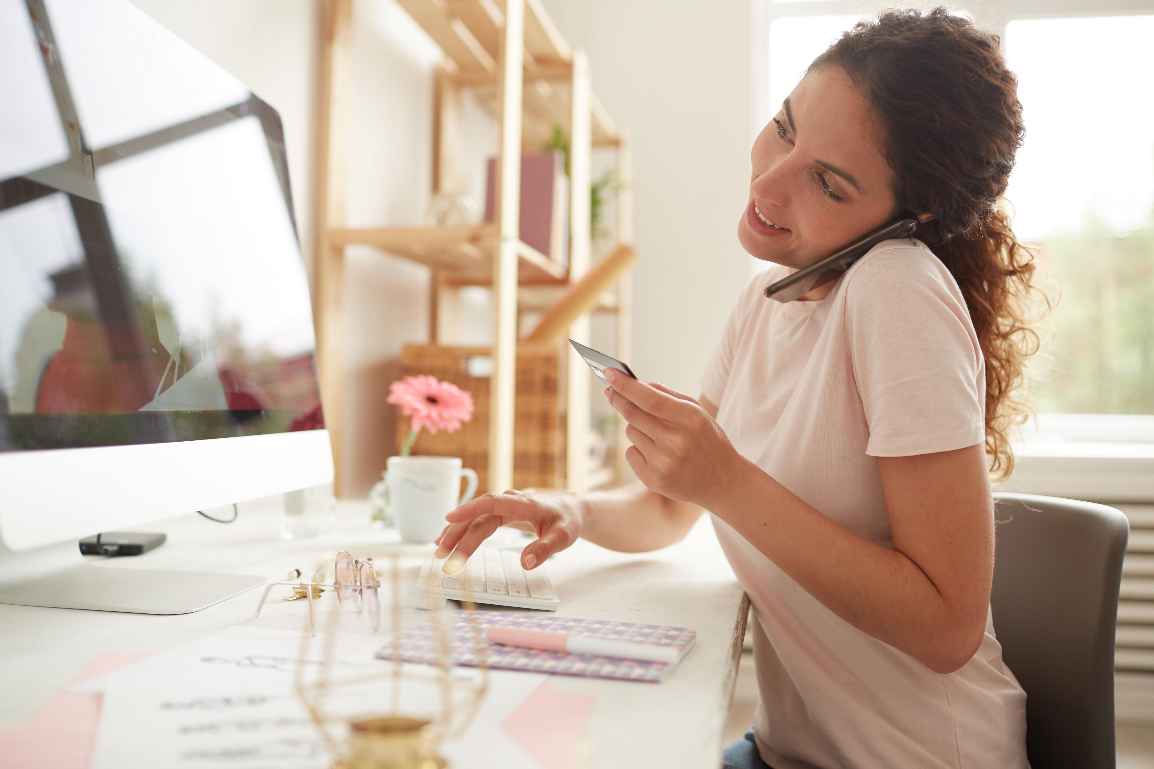 A woman multitasking while on a phone call and entering credit card details into her computer, representing a dynamic and engaged professional setting, ideal for a "social media ad agency.