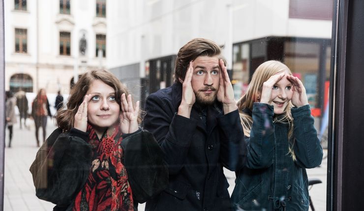 Foto von drei Studierenden die durch ein Fenster in das Hörsaalgebäude gucken