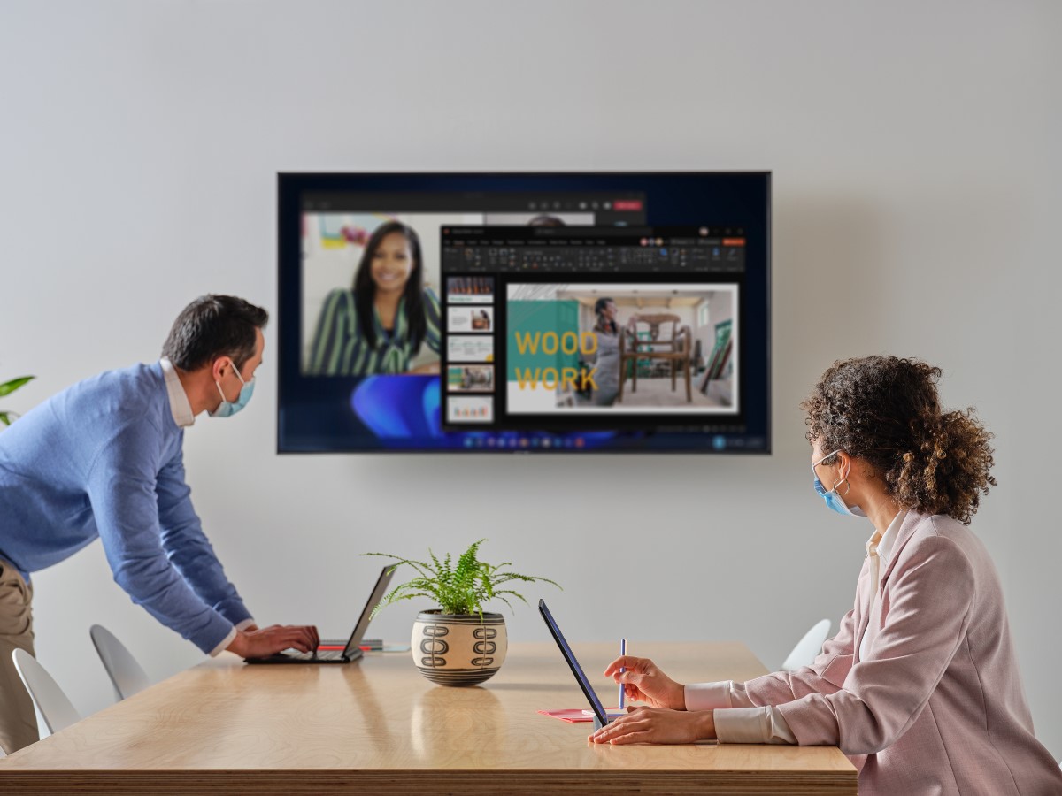 Coworkers with masks setting up a Microsoft Teams meeting in a conference room with their HP Elite Folio Notebooks.