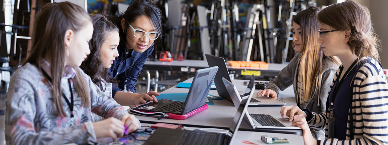 Insegnante femminile con un gruppo di giovani ragazze che lavorano sui loro computer