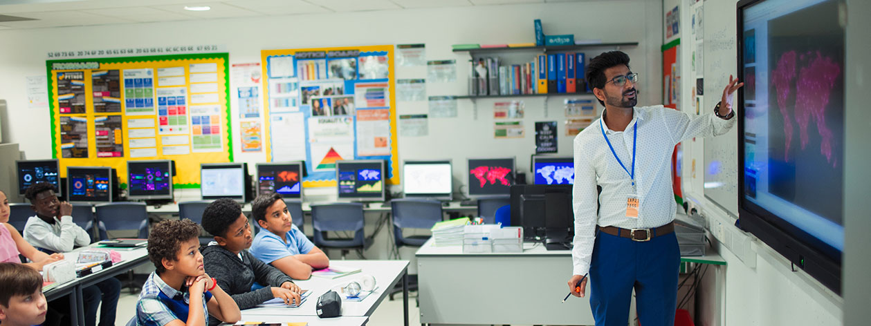 A teacher pointing to a projected screen in a classroom