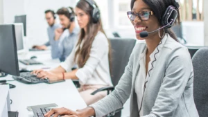 Customer service agents sitting with headsets at laptops smiling.