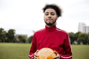 Portrait of a young man holding a ball in a park.