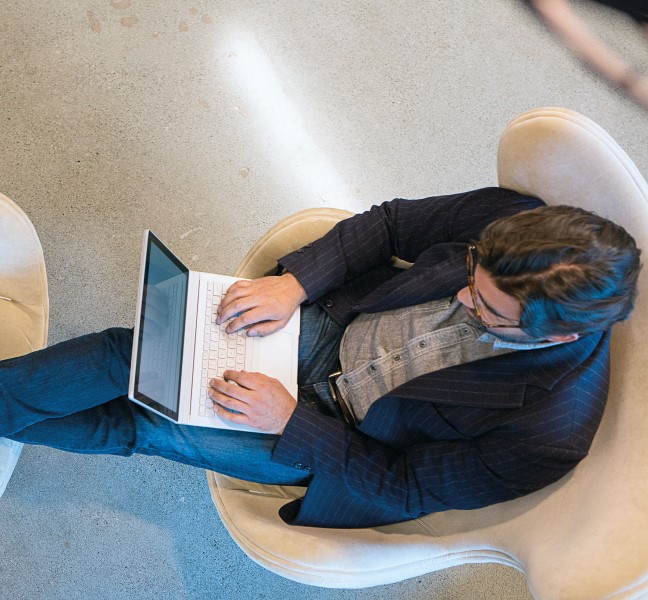 Businessman in office building lounging on chairs with laptop.