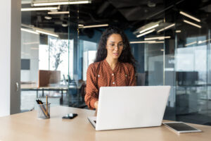 Cheerful and successful indian woman programmer at work inside modern office, tech support worker with laptop typing on keyboard smiling