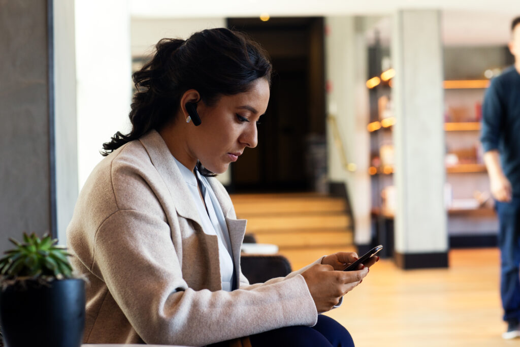 Photo of a female manager sitting in a hotel lobby approving a purchase order on her mobile device.