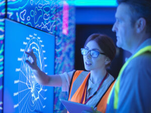 Female geologist with colleague studying graphical display of oil and gas bearing rock on screens.