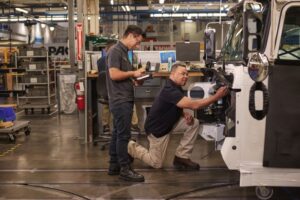 Two engineers wearing safety goggles make repairs at a manufacturing plant.