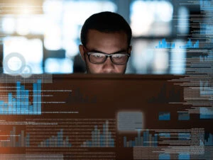 Security worker wearing glasses and looking at a computer monitor, surrounded by an overlay of code and charts.