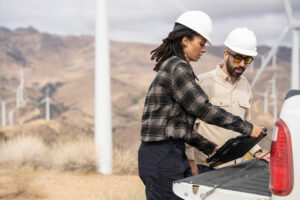 Field engineers using a laptop on truck tailgate to review data after inspection of turbines on a wind farm.