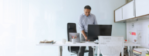 Image of a man standing at his desk and working on his desktop computer.