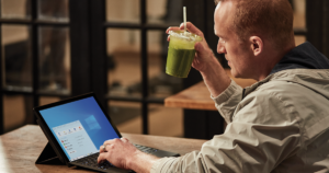 An IT worker holding a smoothie and working on his laptop.