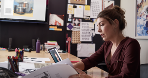 An image of a female small business professional working on designs using devices running PowerPoint and Microsoft Teams.