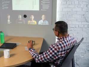 Adult male sitting at conference table looking at screen projected on wall.