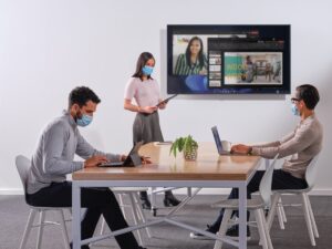 Coworkers setting up a PowerPoint presentation for a Microsoft Teams meeting in a conference room.