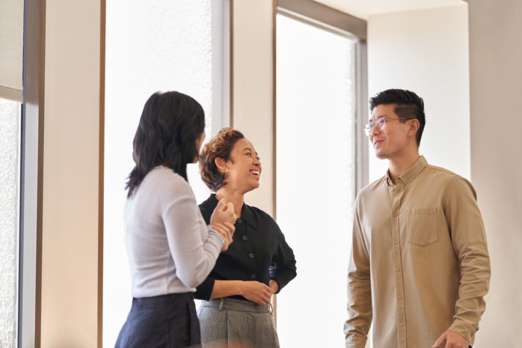 Two women and a man having a conversation standing in an office hallway.