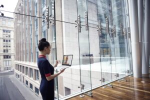 Female business professional standing in larger foyer while holding an open Dell device, running Microsoft Teams.