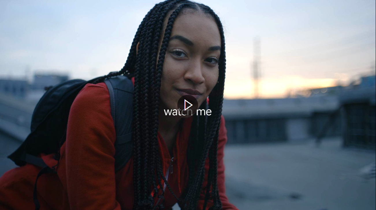 A frame from a video picturing a woman sitting down outdoors, wearing a backpack.