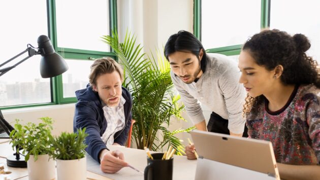 A group of people sitting at a table collaborating on work and using a laptop computer.