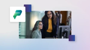 One person standing at the desk of another person sitting, looking at a computer, in an office. The image is overlaid on a soft blue gradient background incorporating the Microsoft Power Platform icon.