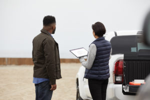 Two adults outside collaborating at a work site while using Microsoft OneNote. Female holding a black Microsoft Surface Pro X in tablet mode with male at her side.