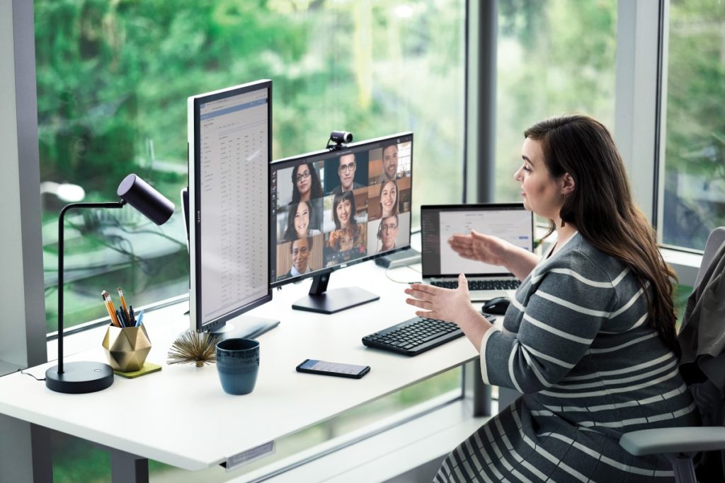 Female enterprise employee working at desk with multiple devices, including HP Elitebook, running a Microsoft Teams conference call.