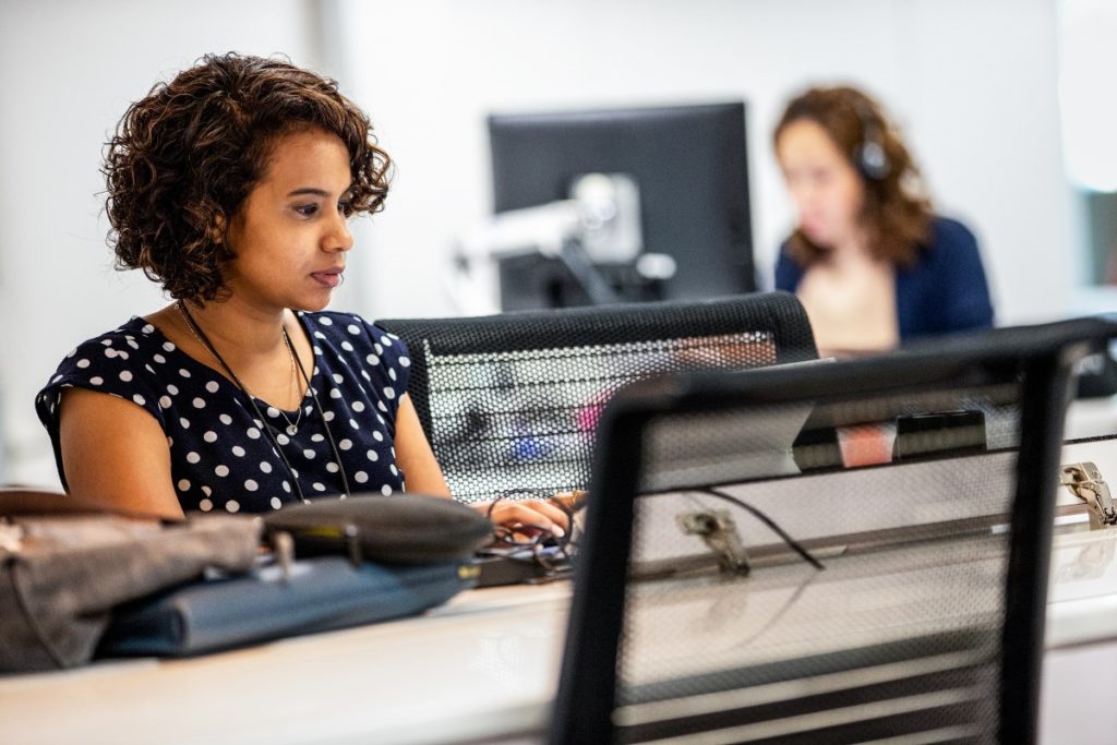 Image of a woman sitting at a computer desk, looking at a monitor