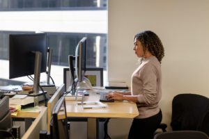 Real people, real offices. Black female developer doing focused work at a standing desk in enterprise workspace.